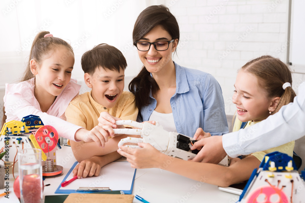Poster three elementary school students are learning about robotics with their teacher. the teacher is hold
