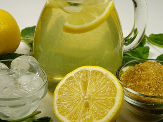 Glass jug  with freshly prepared homemade lemonade and ingredients   for making lemonade. Lemons,...