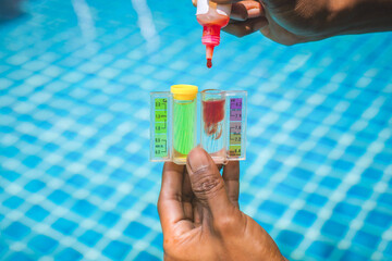 Action of a person hand is using Phenol red droplet to drop into sample water for measuring the pH value. Swimming pool water treatment service and maintenance.