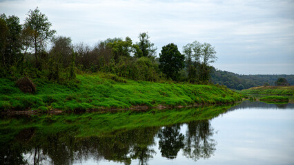 Fototapeta premium A beautiful riverbank with lush greenery and calm water reflection, creating a serene atmosphere