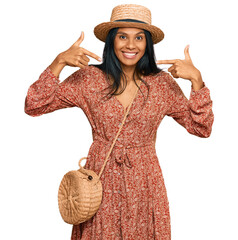 Young african american woman wearing summer hat looking confident with smile on face, pointing...