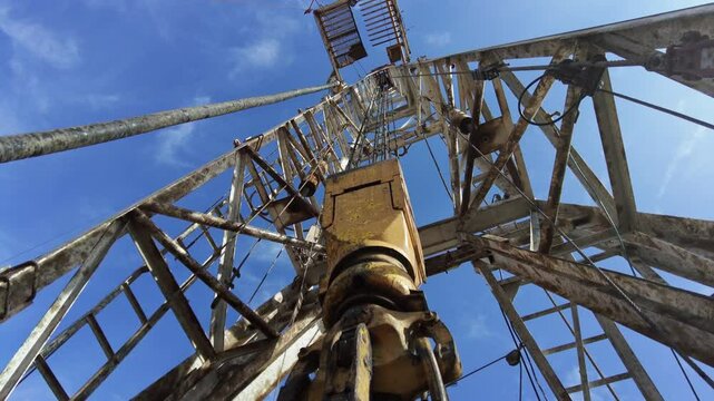 Borer vibrates as it drills ground. Footage at the base of a high derrick at the site for production oil. Low angle view.