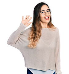 Beautiful hispanic woman wearing casual sweater and glasses waiving saying hello happy and smiling, friendly welcome gesture © Krakenimages.com