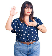 Young plus size woman wearing casual clothes swearing with hand on chest and open palm, making a...