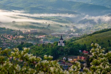 Small town in a valley surrounded by hills and meadows with fog at sunrise and the romantic...