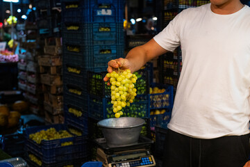 Grapes on the market stall. Man holding bunch of grapes.