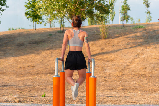 Young woman working out on parallel bars in outdoor park