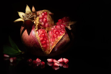 Close-up of a wild pomegranate that has burst open. The seeds glow red against a dark background.