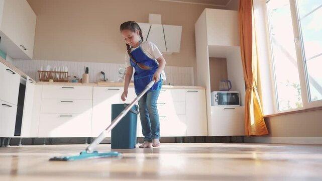 the child baby washed the floors. happy family kid dream concept. daughter washed the floors with a mop in indoors the kitchen in an apron helps mom. mom asked the child girl to mop the floors