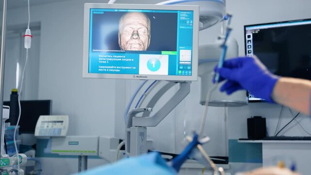 Doctor's hand wearing blue latex glove holding a surgical probe tool. Screen with 3d image of patient's head at backdrop.