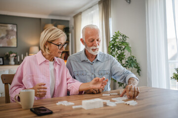 Senior couple husband and wife play dominoes together at home