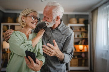 Senior couple use mobile phone together at home