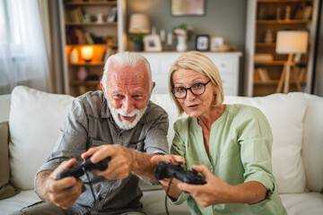 Senior couple sit on sofa and play video games on joystick at home