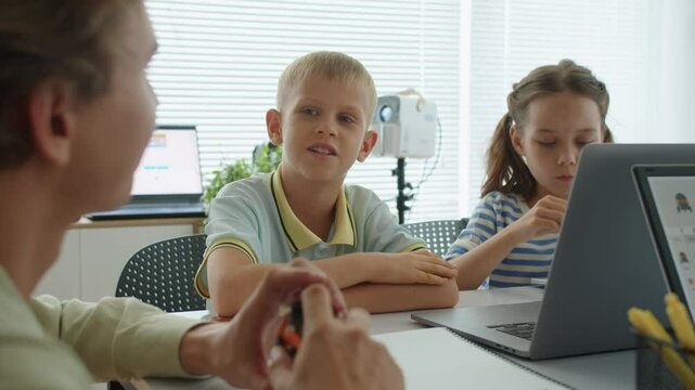 Handheld shot of male tutor holding robot model when talking to kids during engineering class