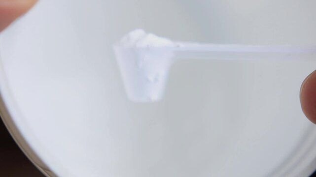 A person take a scoop from a white creatine for inspection
