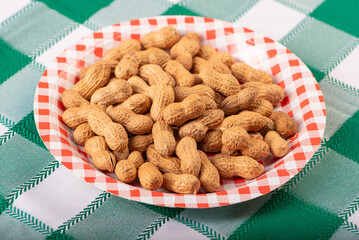 Peanuts, portion of peanuts in shell on a plate, on a green and white checkered tablecloth. Selective focus.