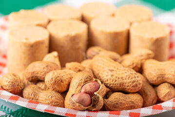 Peanuts, portion of peanuts in shell and paçoquinha (peanut candy) on a plate, on a green and white checkered tablecloth. Selective focus.