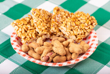 Peanuts, portion of shelled peanuts and pé-de-moleque (peanut candy) on a plate, on a green and white checkered tablecloth. Selective focus.
