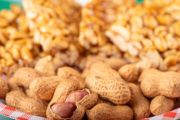 Peanuts, portion of shelled peanuts and pé-de-moleque (peanut candy) on a plate, on a green and white checkered tablecloth. Selective focus.
