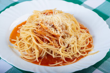 Pasta, portion of spaghetti noodles with grated cheese on a white plate on a green and white checkered tablecloth. Selective focus.