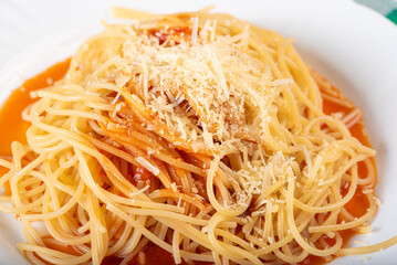 Pasta, portion of spaghetti noodles with grated cheese on a white plate on a green and white checkered tablecloth. Selective focus.