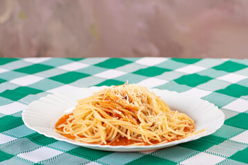 Pasta, portion of spaghetti noodles with grated cheese on a white plate on a green and white checkered tablecloth. Selective focus.