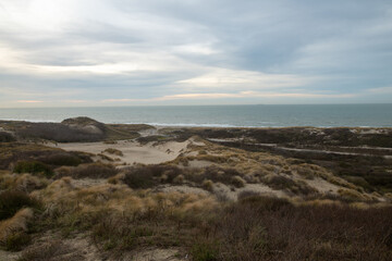 A sweeping sand dune under a dramatic, cloud-filled sky, with shifting shadows and soft light filtering through the clouds