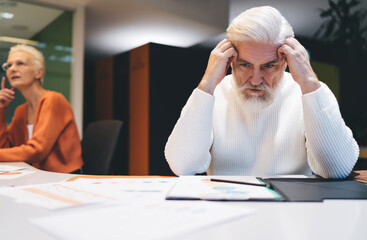 Depressed Senior man deeply engrossed in work, looking stressed while reviewing documents at office...