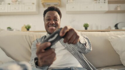 Happy African American student playing video game in apartment, male portrait. Entertainment and pastime in weekend, internet and game addiction of modern people, player scoring goal and rejoicing