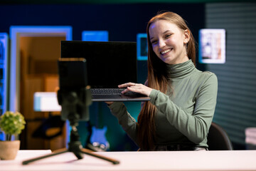 Joyous teenager presenting laptop from brand sponsoring video, urging subscribers to purchase it,...
