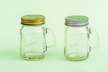Glass salt and pepper shakers with metal lids placed on a vibrant green background adding a touch of color and elegance to kitchen essentials.