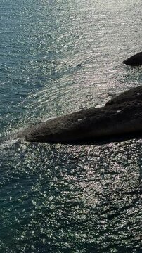 Sea dark blue glittering water and coastal rocks, vertical video.