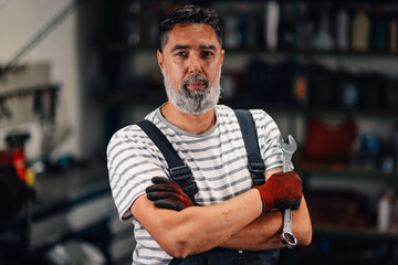 Repairman with arms crossed holding a wrench at mechanic workshop.