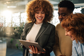 Interracial business team smiling at tablet at minimalistic workspace.