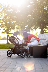 Young mother with her cute baby is sitting on a park bench