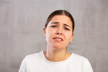 Close-up portrait of young woman with sad expression on face against light unicoloured background