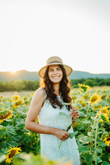 One beautiful young caucasian woman is in sunflower field checking on plants and sunflowers during the day