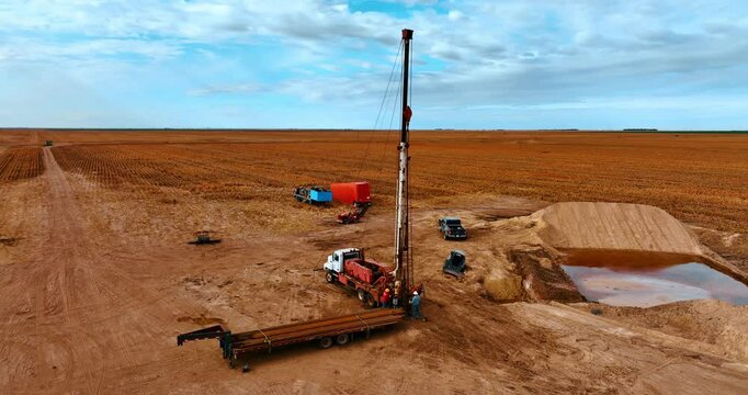 Site in the field with orange ground used at oil production. Two men work at the truck with derrick for drilling.