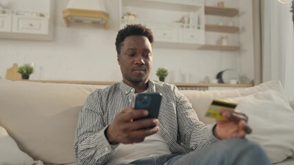 Pay by card in online services, African man inputting data of credit card in app . Internet fraud and data theft, cybercrime and cyber security, young adult black male person shopping online from home