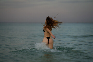 Fototapeta premium Sexy woman enjoying summer at sea. Beautiful girl in a sexy bikini on the beach. Sexy booty woman playful on paradise tropical beach. Summer girl running and splashing in sea water.