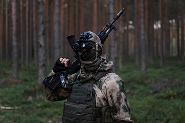A soldier in camouflage, with a night vision binocular on his head and modern AK 12 rifle in his...