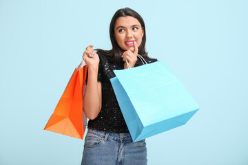 Beautiful young thoughtful woman with shopping bags on blue background