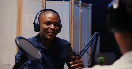 African american man recording podcast using high tech audio equipment to interview guest, ensuring...