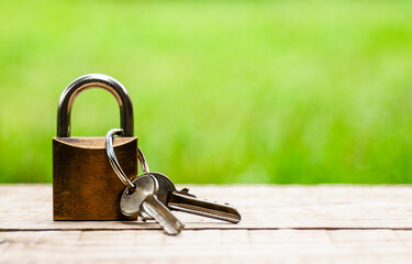 Lock with keys on wooden table on blurred natural background. Copy space