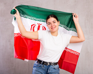 Joyous young woman with Iran flag in hands posing happily against light unicoloured background