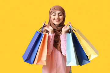 Happy Muslim woman with shopping bags on yellow background