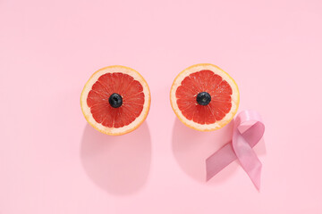 Halves of ripe grapefruit and pink ribbon on color background. Breast cancer awareness concept