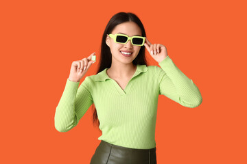 Beautiful young Asian woman with chewing gum on orange background