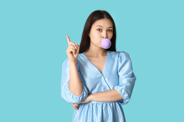 Beautiful young Asian woman with chewing gum on blue background