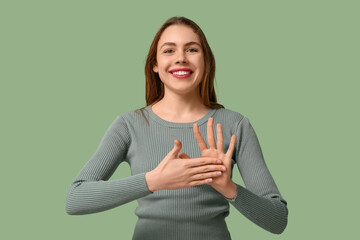 Young deaf mute woman using sign language on green background